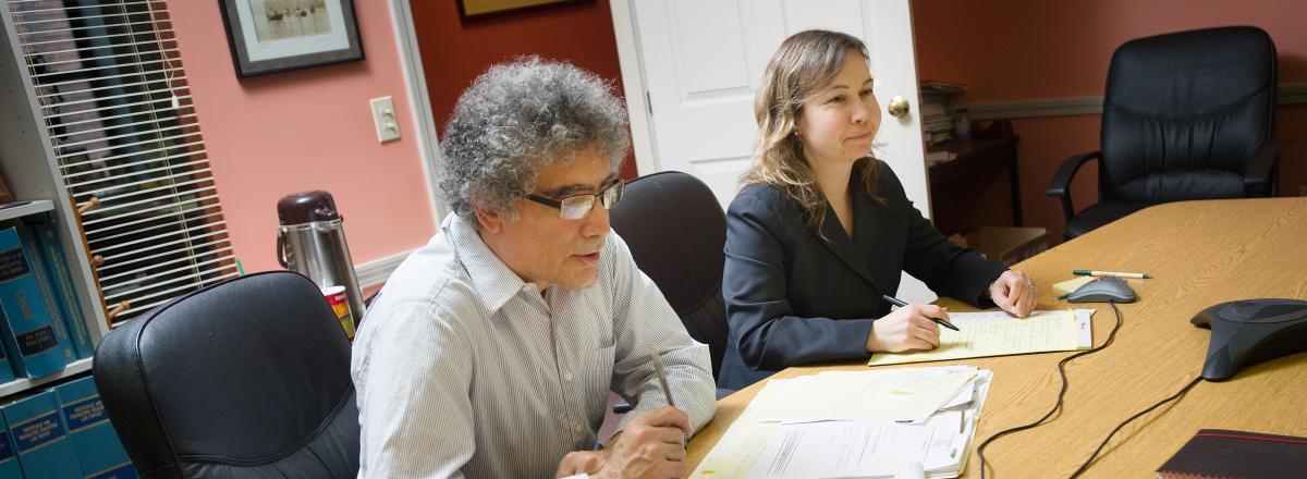 A picture of two PTLA attorneys, Frank and Katie, sitting at a conference table in a library, looking at legal papers